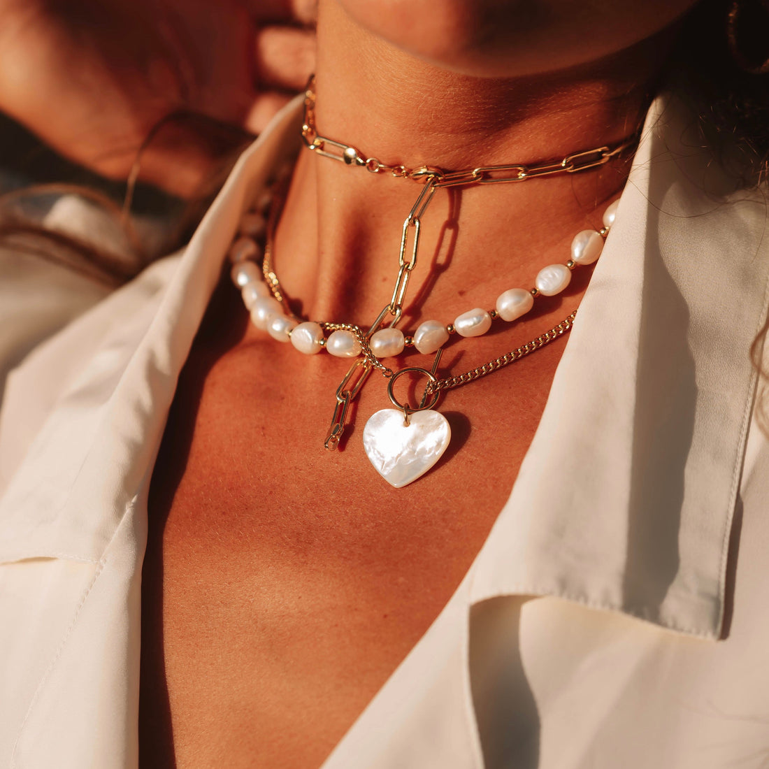 Layered pearl and gold necklaces styled with a white shirt in warm sunlight
